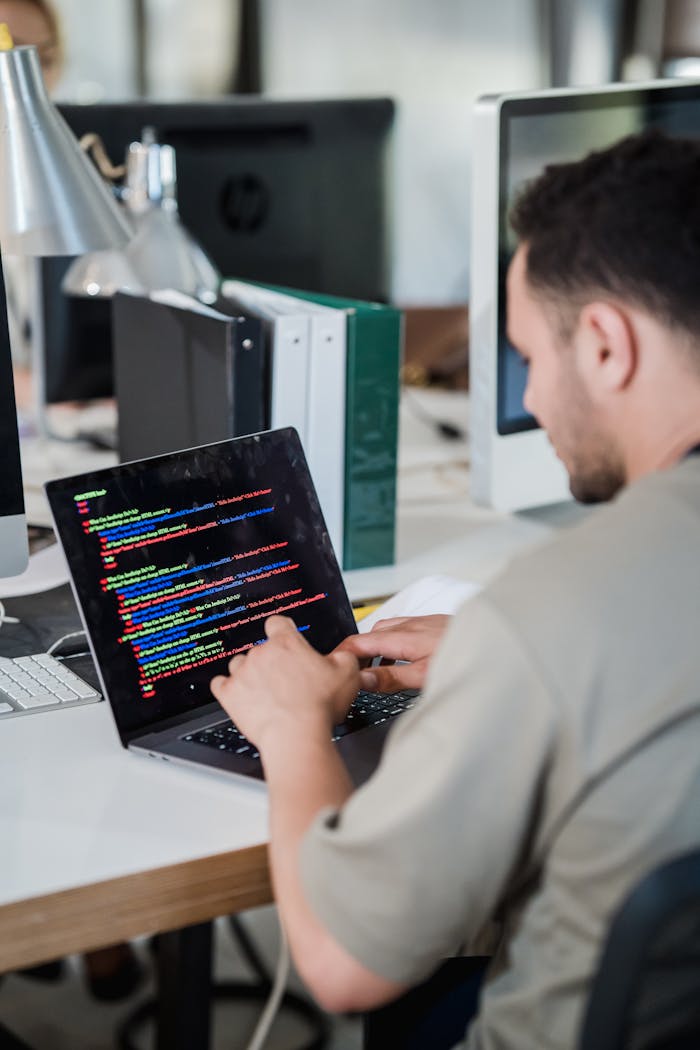 Focused software developer typing code on a laptop in a modern office setting.
